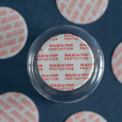 Vista cercana de un sello sensitivo tipo pressure sensitive con impresión “Sealed for your protection” en inglés, adherido a la boca de un frasco. Producto de seguridad desarrollado por Sellaempaq para proteger medicamentos, suplementos y productos cosméticos contra manipulaciones.